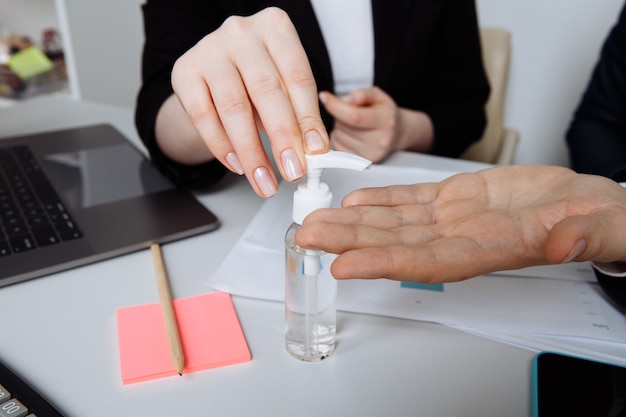 Primer plano de las manos con gel antiséptico para desinfectar las manos sobre un escritorio en una oficina.