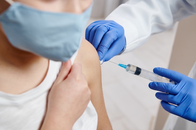 Primer plano de manos con guantes protectores médicos sosteniendo la jeringa y haciendo la inyección de la vacuna en el brazo de un niño