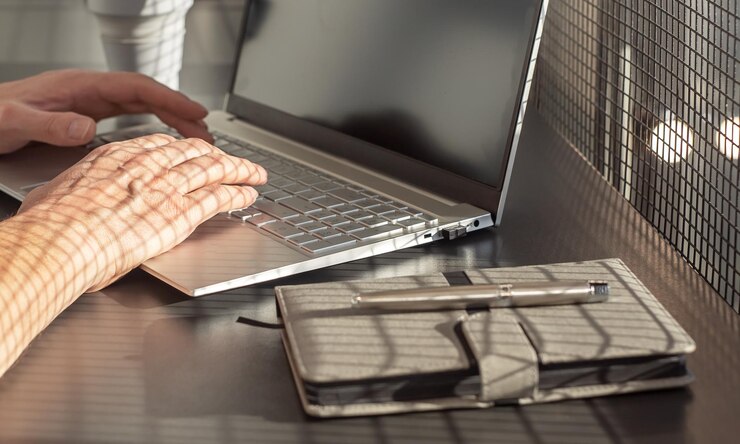 Foto primer plano de las manos del hombre escribiendo en el teclado de la computadora portátil empresario sentado en la oficina o en el escritorio de la casa con un diario