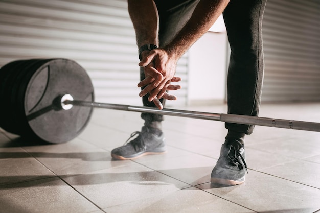 Primer plano de las manos de un hombre fuerte preparándose para levantar pesas en el gimnasio del garaje.