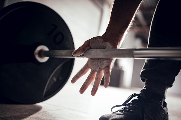 Primer plano de las manos de un hombre fuerte con talco preparándose para levantar pesas en el gimnasio del garaje.