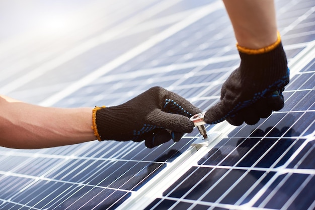 El primer plano de las manos del hombre con guantes negros con una llave en las manos instalando paneles solares