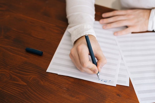 Foto primer plano de las manos del hombre irreconocible escribiendo notas musicales con lápiz en partituras