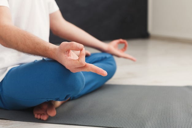 Primer plano de manos de hombre irreconocible, meditando, sentado en posición de loto en la estera, espacio de copia