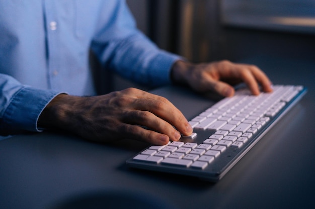 Primer plano de las manos de un hombre irreconocible que escribe un mensaje en la red social. Vista de cerca del desarrollo de la programación y la codificación en el teclado inalámbrico trabajando a altas horas de la noche. Concepto de trabajo remoto.