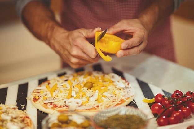 Foto primer plano de las manos de un hombre joven cortando pimentón y poniendo la masa de pizza.