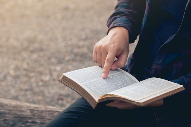 Primer plano de las manos del hombre mientras lee la Biblia afuera