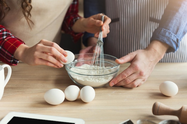 Primer plano de manos de hombre y mujer batiendo huevos y hornear pasteles en la cocina tipo loft. Pareja irreconocible cocinando masa juntos, espacio de copia