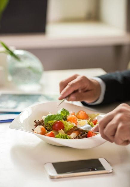 Primer plano de las manos de un hombre de negocios sosteniendo un cuchillo y un tenedor sobre la ensalada durante el almuerzo de negocios