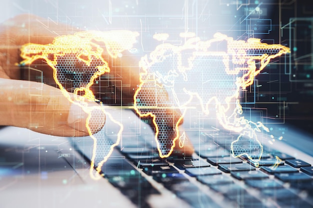 Primer plano de las manos del hombre de negocios usando el teclado de la computadora portátil con holograma de mapa dorado brillante abstracto sobre fondo borroso Mundo digital y concepto de tecnología Doble exposición