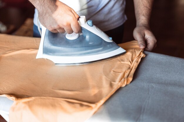 Primer plano de las manos de un hombre planchando una camiseta. Feminismo