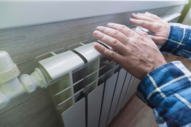 Primer plano de las manos de un hombre que las calienta sobre una batería blanca El concepto de problemas con la calefacción en la crisis energética de invierno