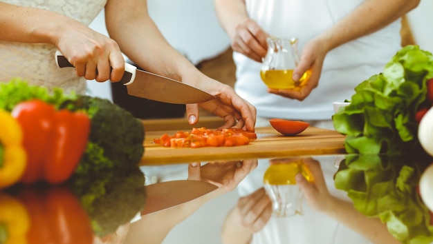 Primer plano de manos humanas cocinando en la cocina. Madre e hija o dos amigas cortando verduras para ensalada fresca. Conceptos de amistad, cena familiar y estilo de vida.