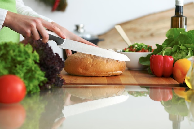 Primer plano de manos humanas cocinando en la cocina sobre la mesa de cristal con reflejo. Ama de casa rebanando pan.