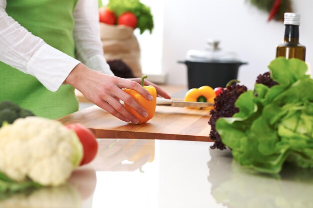 Primer plano de manos humanas cocinando ensalada de verduras en la cocina en la mesa de cristal con reflejo. Comida saludable y concepto vegetariano.