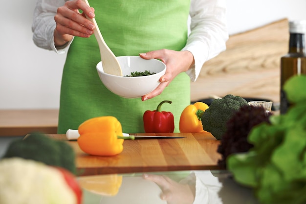 Primer plano de manos humanas cocinando ensalada de verduras en la cocina en la mesa de cristal con reflejo. Comida saludable y concepto vegetariano.