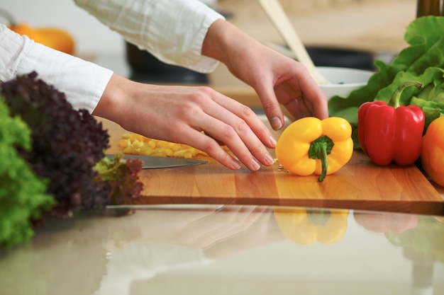 Primer plano de manos humanas cocinando ensalada de verduras en la cocina en la mesa de cristal con reflejo. Comida saludable y concepto vegetariano.