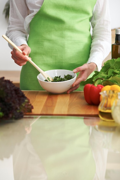Primer plano de manos humanas cocinando ensalada de verduras en la cocina en la mesa de cristal con reflejo. Comida saludable y concepto vegetariano.