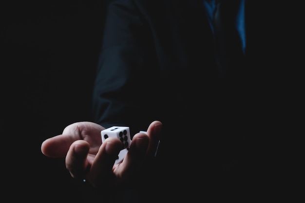Primer plano de las manos de un joven empresario y hombre de negocios en traje formal ropa rodando dados en un fondo oscuro
