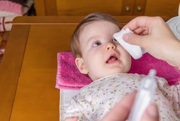 Primer plano de las manos de la madre limpiando los ojos del bebé con suero fisiológico en un algodón