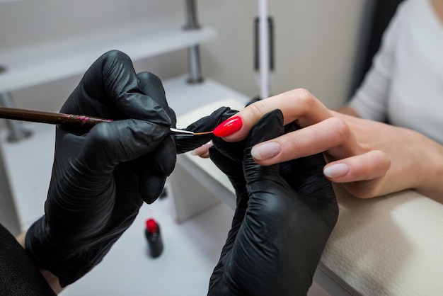 El primer plano de las manos de una manicurista pinta las uñas de un cliente con barniz rojo