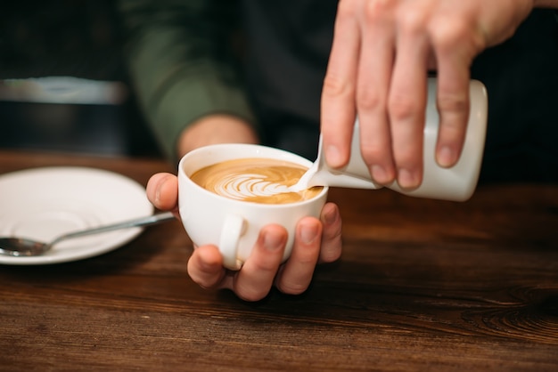 Primer plano de manos masculinas añadiendo crema al café.