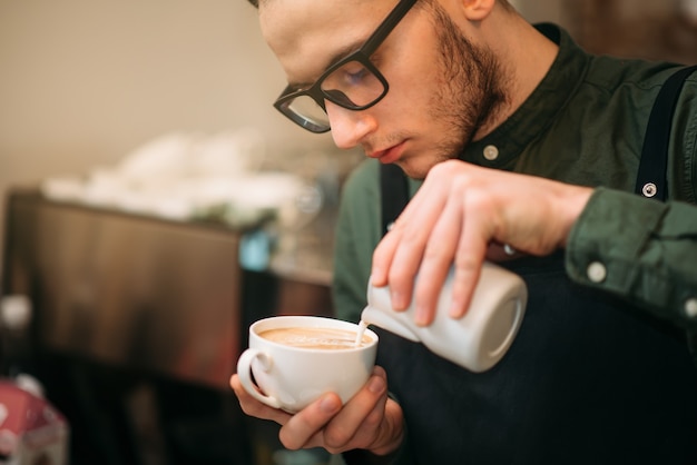 Primer plano de manos masculinas añadiendo crema al café.