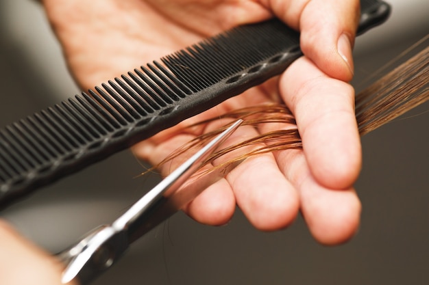 Primer plano de las manos masculinas de peluquería durante el corte de cabello femenino