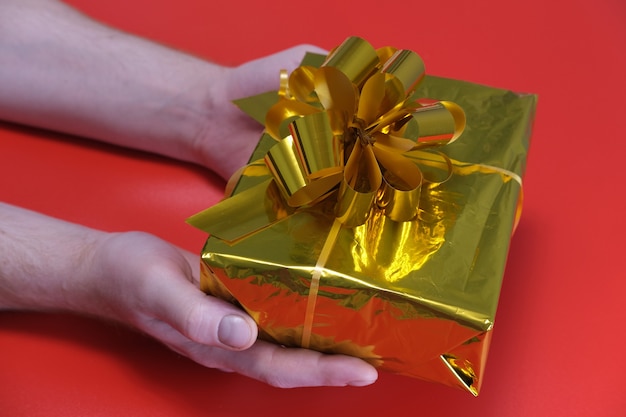 Primer plano de manos masculinas sobre un fondo rojo. El hombre sostiene una caja con un regalo en la mano. Concepto para Navidad, Año Nuevo 2022, Viernes Negro.