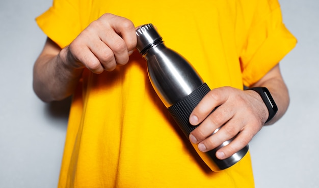 Primer plano de manos masculinas sosteniendo una botella de agua termo de acero.