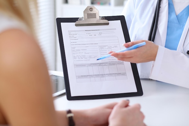 Foto primer plano de las manos de un médico y un paciente mientras el médico señala el formulario de historial médico en el portapapeles. concepto de medicina y atención de la salud.