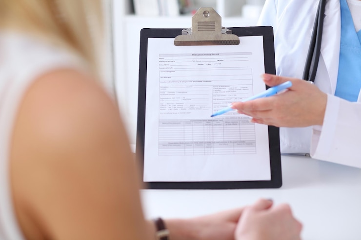 Foto primer plano de las manos de un médico y un paciente mientras el médico señala el formulario de historial médico en el portapapeles. concepto de medicina y atención de la salud.