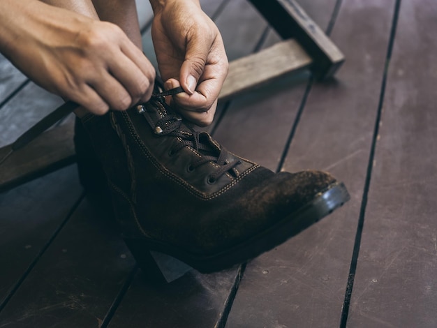 Primer plano de las manos de la mujer atando los cordones de los zapatos en las viejas botas de cuero en sus piernas mientras se sienta en una silla de madera en la terraza de tablones de madera