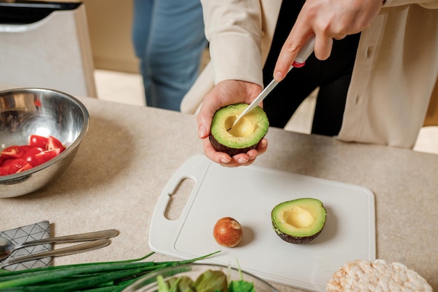 Primer plano de las manos de la mujer cortando aguacate fresco en la cocina moderna Nutrición y dieta Concepto de comida saludable Ingredientes para batidos