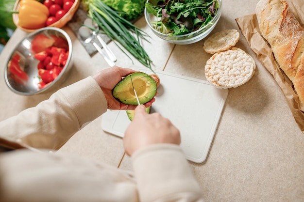 Primer plano de las manos de la mujer cortando aguacate fresco en la cocina moderna Nutrición y dieta Concepto de comida saludable Ingredientes para batidos