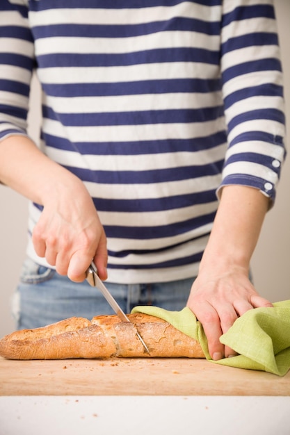 Primer plano de manos de mujer cortando baguette francesa en la mesa Cocinar y servir comida en casa