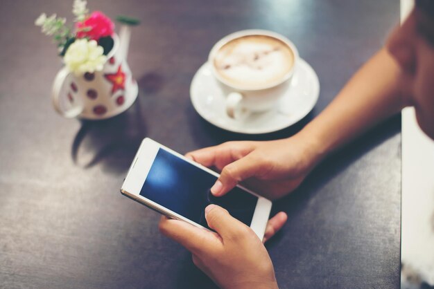 Primer plano de las manos de una mujer enviando mensajes de texto con su móvil en una cafetería