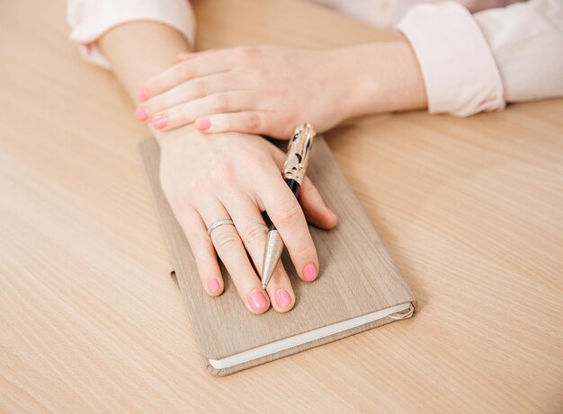 Primer plano de las manos de una mujer escribiendo en un bloc de notas colocado en una mesa de madera oficina en casa y planes de concepto de trabajo y reunión de negocios