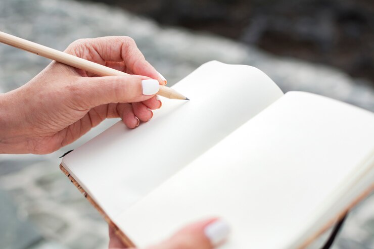 Primer plano de las manos de una mujer escribiendo en su cuaderno con un lápiz de madera.
