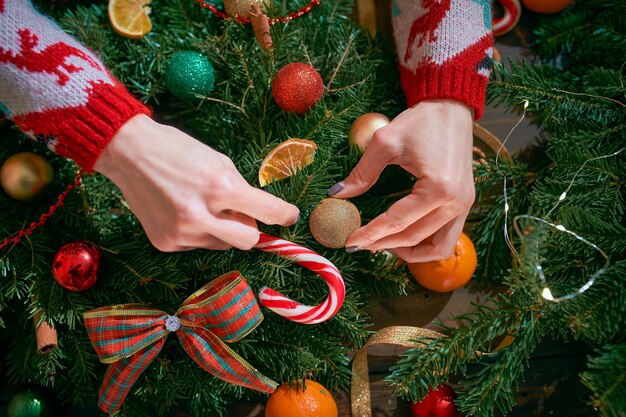 Primer plano de las manos de una mujer haciendo corona de Navidad hecha a mano en la mesa para las vacaciones.