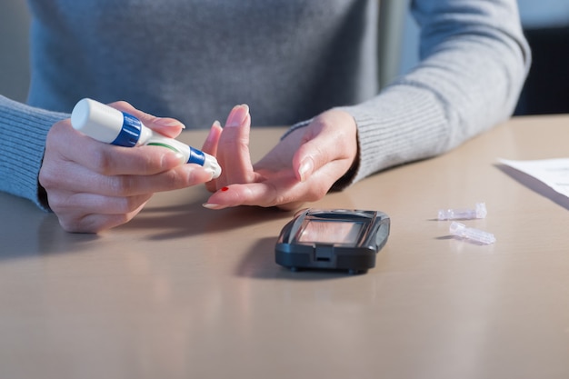 Primer plano de manos de mujer con lanceta en el dedo para comprobar el nivel de azúcar en la sangre con el medidor de glucosa