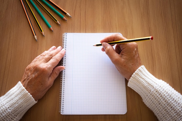 Primer plano de manos de mujer madura con lápiz escribiendo en el cuaderno