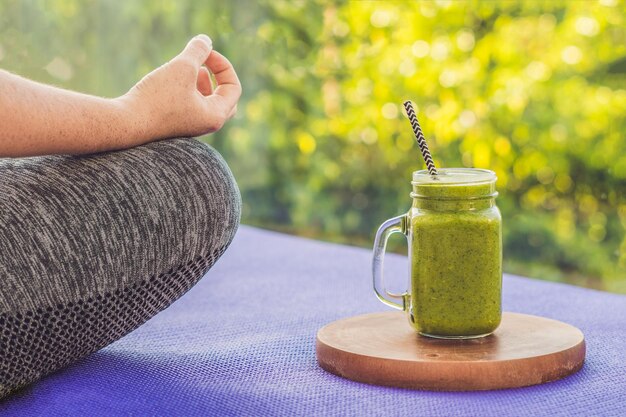 Primer plano de las manos de una mujer durante la meditación con batidos verdes de espinacas, naranja y plátano