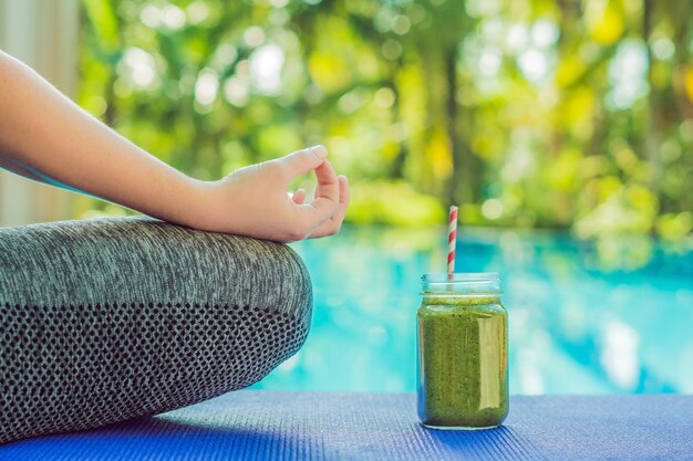 Primer plano de las manos de una mujer durante la meditación con un verde batidos de espinacas, naranja y plátano en el fondo de la piscina