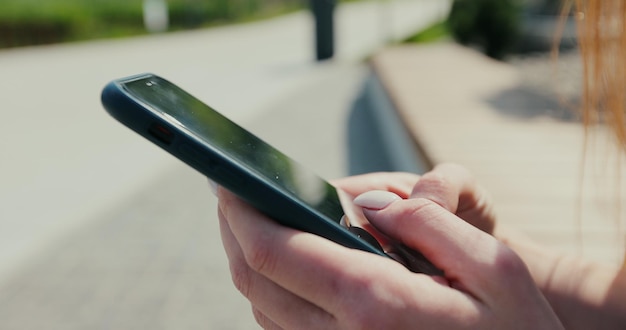 Primer plano de manos de mujer con mensajero de mensajes de texto de teléfono inteligente en el banco de la calle