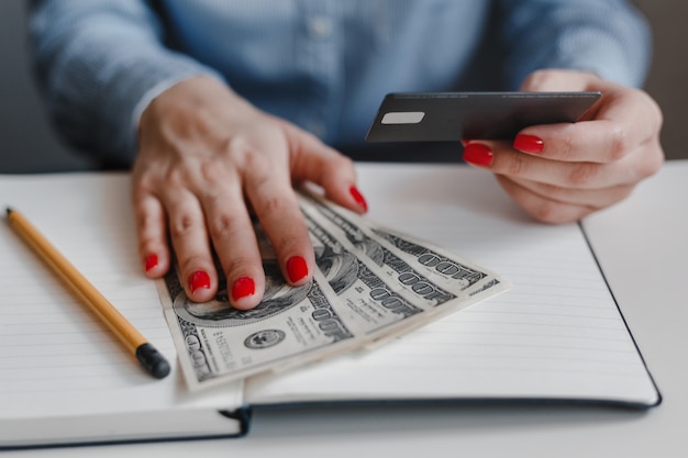 Foto primer plano de las manos de una mujer con uñas rojas sosteniendo billetes de cien dólares y una tarjeta de crédito negra