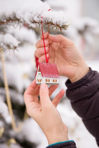 Primer plano de manos de mujer sosteniendo la decoración de la casa de Navidad y decorando el árbol al aire libre