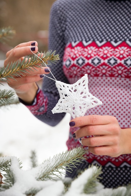 Primer plano de las manos de una mujer sosteniendo un juguete de Navidad de estrella blanca y decorando el árbol de Navidad