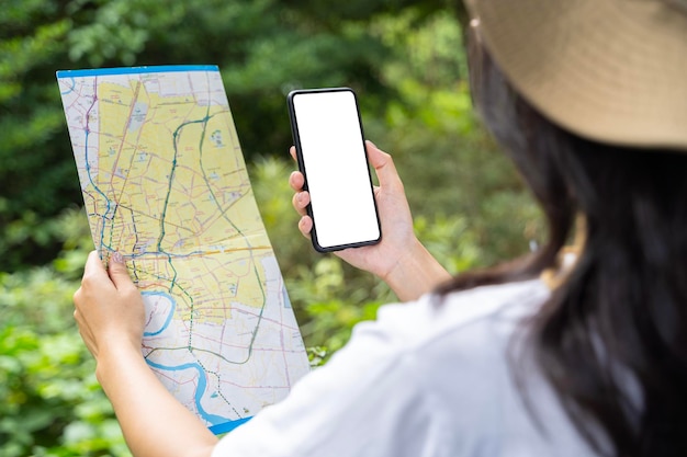 Primer plano de las manos de una mujer con un teléfono inteligente y un mapa en el fondo del bosque aislando la pantalla Una joven feliz con un teléfono inteligente con un mapa viajando por la naturaleza Concepto de viaje