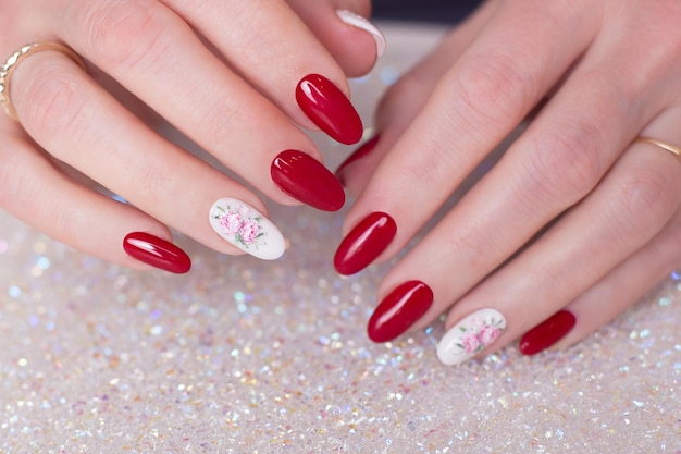 Un primer plano de las manos de una mujer con uñas rojas y un diseño floral rosa y blanco en ellas